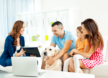 Young couple with their toddler and dog sitting on a couch going over something on a tablet with an agent