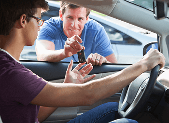 parent handing their teen driver car keys through the open driver side window of a car
